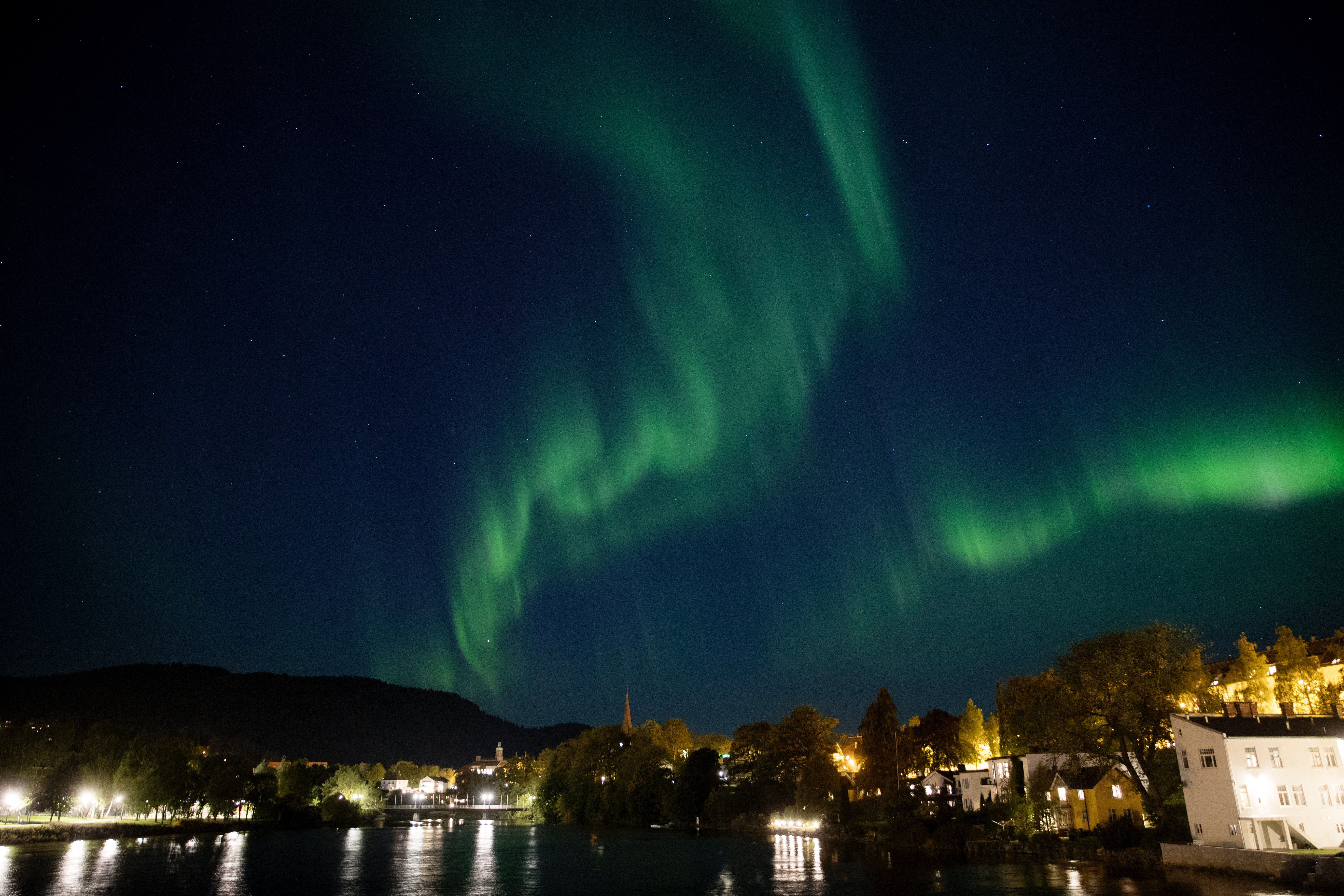 Grønt nordlys over nattehimmelen, med Nidelva og bebyggelsen på Kalvskinnet nedenfor